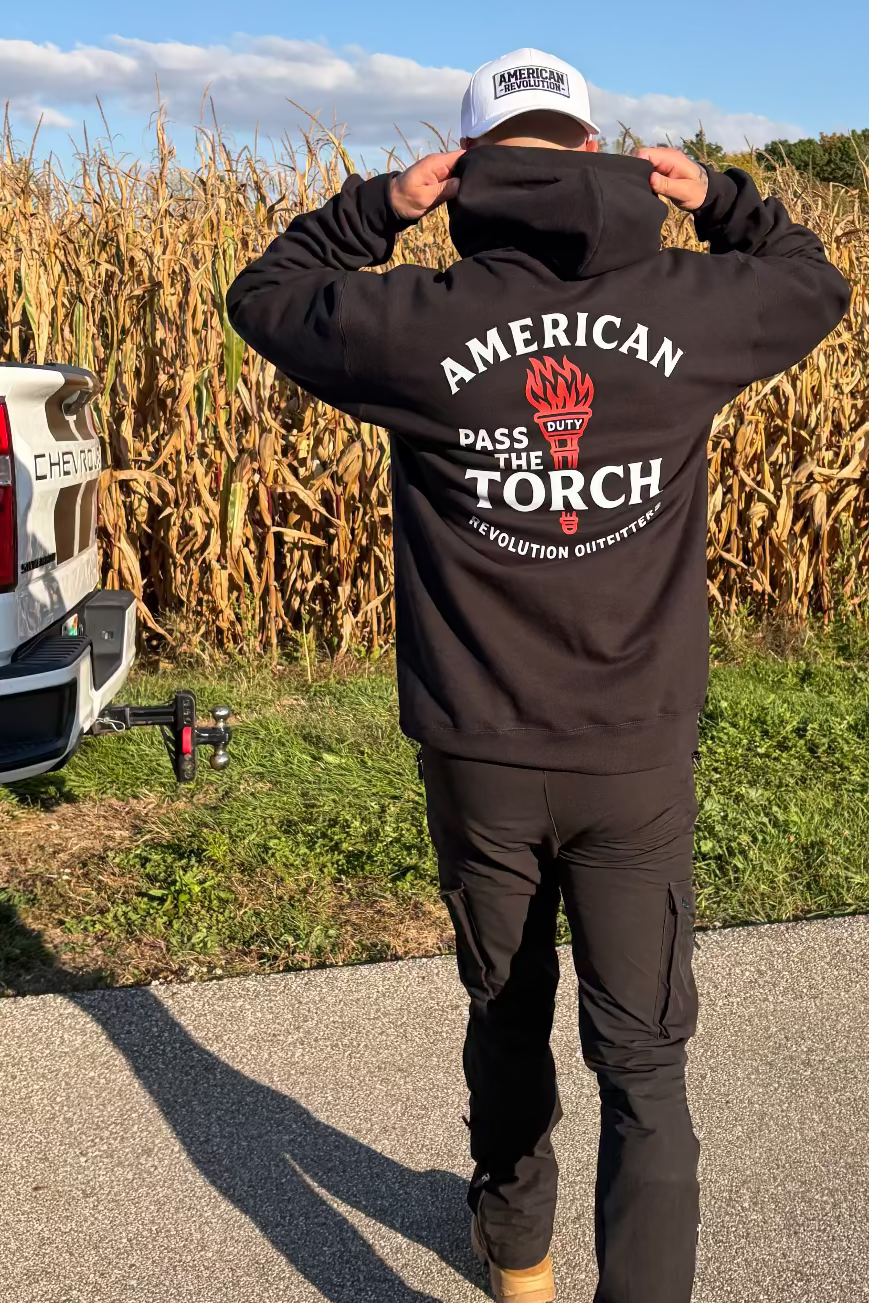 Man wearing a black hoodie with 'American Made the Torch' logo in a cornfield