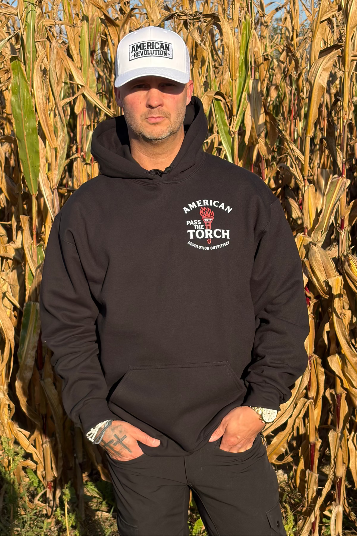 Man wearing a black hoodie with 'American Made the Torch' logo in a cornfield