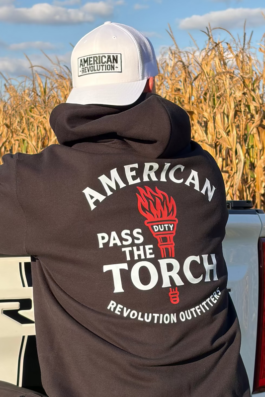Man wearing a black hoodie with 'American Made the Torch' logo in a cornfield