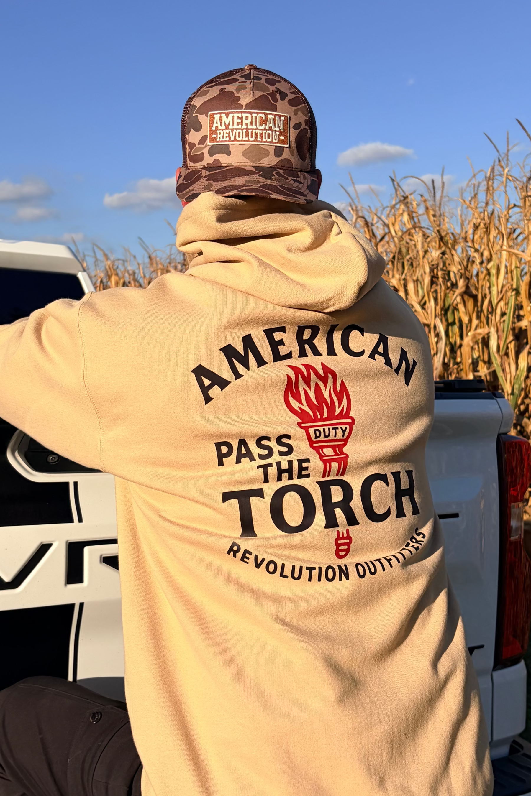 Person wearing a beige hoodie with 'American Torch' logo walking through a cornfield.