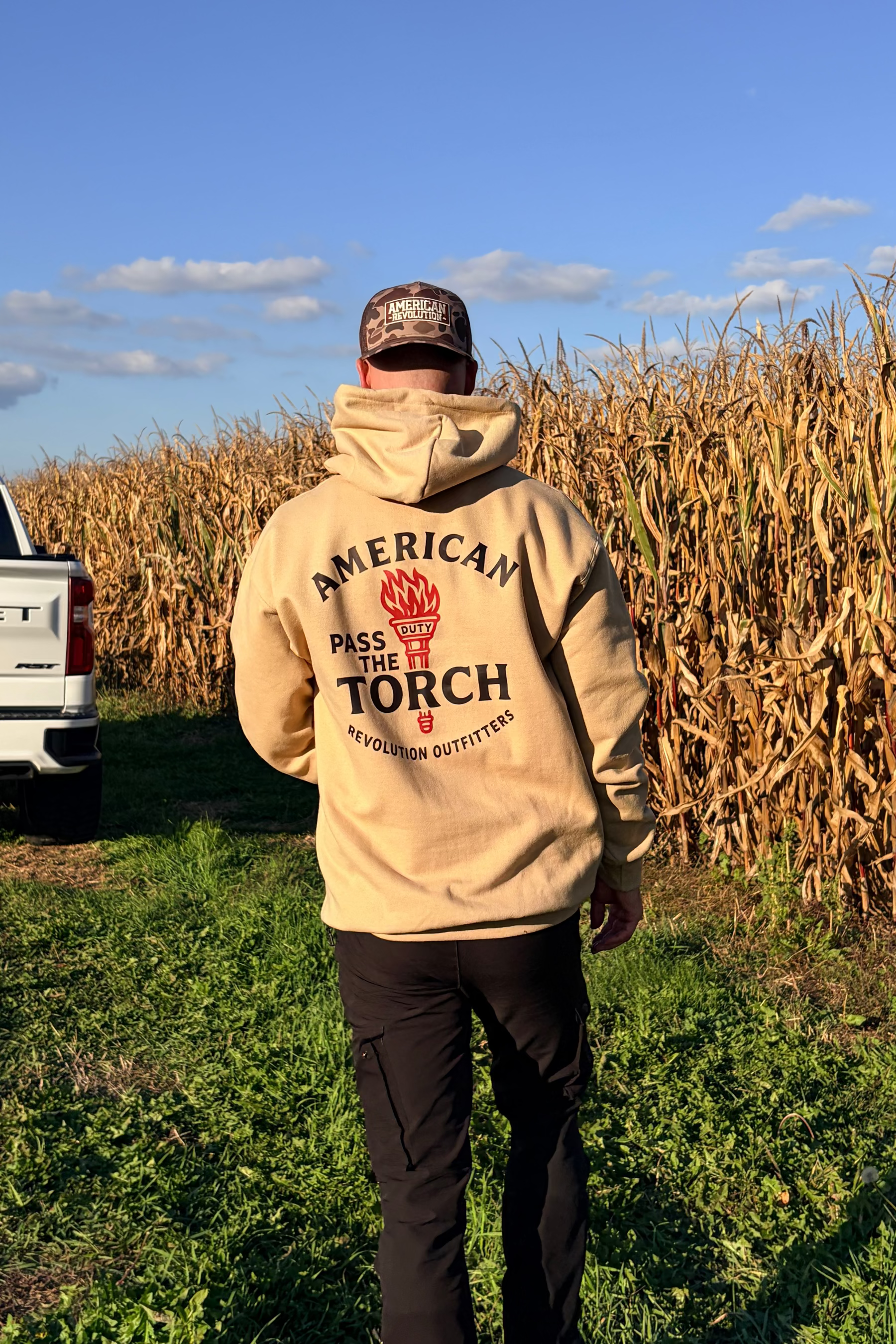 Person wearing a beige hoodie with 'American Torch' logo walking through a cornfield.