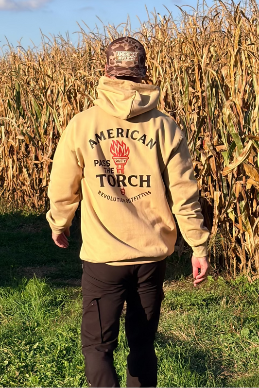 Person wearing a beige hoodie with 'American Torch' logo walking through a cornfield.